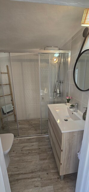 Ein modernes Badezimmer mit einer Duschkabine, einem Holzbadezimmermöbel, einem runden Spiegel und einer Toilette.