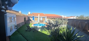 A backyard with a swimming pool, green artificial grass, and a patio with chairs.
