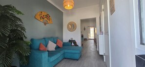 Ein Wohnzimmer mit einem türkisfarbenen Sofa, einem Ventilator und einer großen Pflanze.