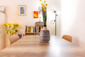 A dining table with a vase of yellow flowers, a bookshelf with books, and framed artwork on the wall. - Apartment 'Marina Formosa' with Shared Pool, Wi-Fi and Air Conditioning (Olhão)