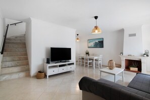 Una sala de estar moderna con televisor de pantalla plana, muebles blancos, una escalera y una chimenea.