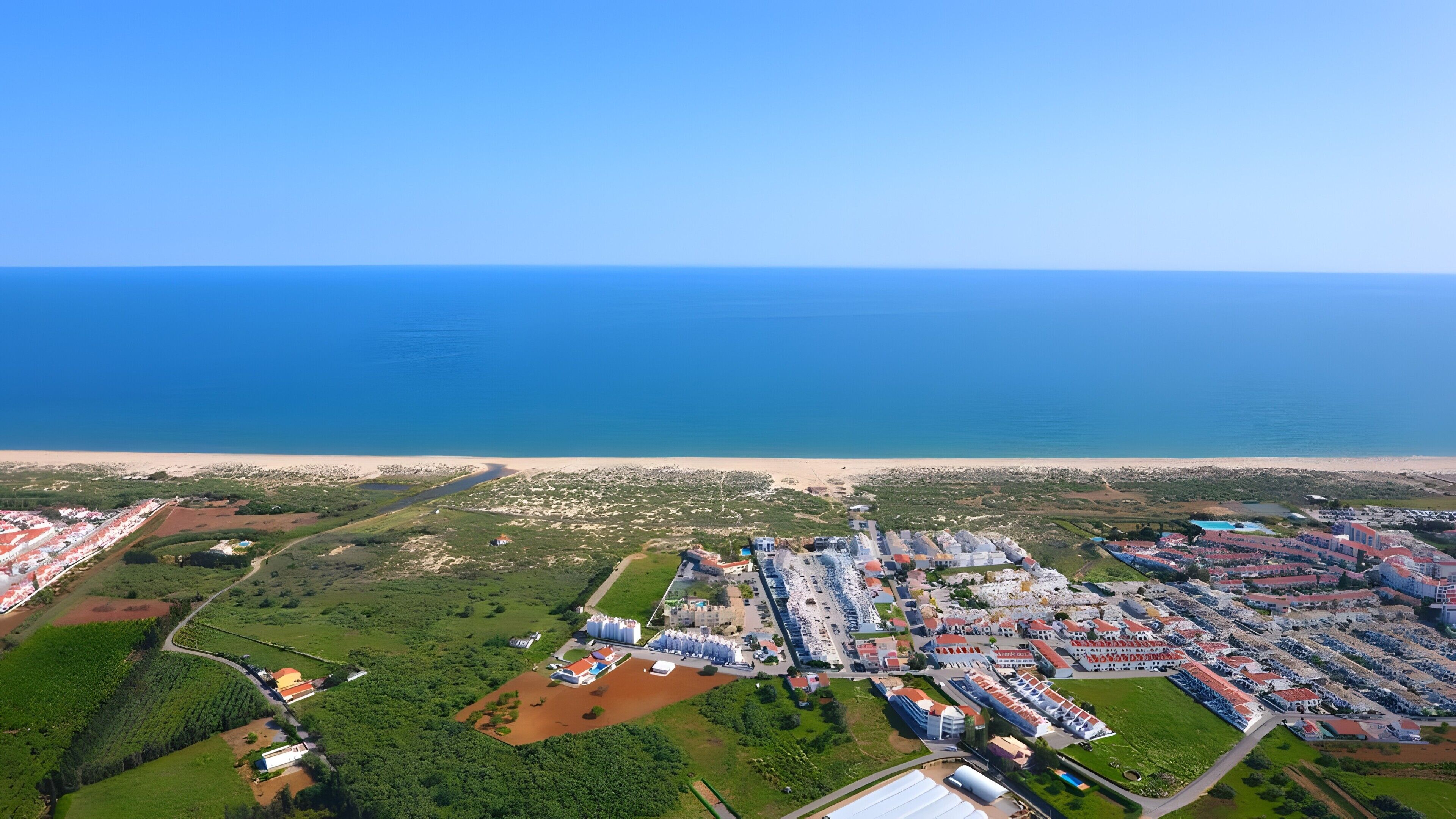 Vista aérea de un resort costero con playa, zonas verdes y un estacionamiento.