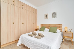 A bedroom with a large wardrobe, a bed with two pillows, and a bedside table with a lamp and a decorative item.