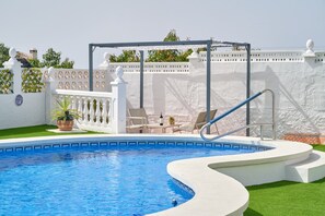 A swimming pool with a white deck, a pergola, and a white fence with decorative elements.