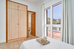 A bedroom with a bed, a wooden wardrobe, a bathroom, and a view through a large window. - Villa 'Grayce' with Mountain Views, Wi-Fi and Air Conditioning (Frigiliana)