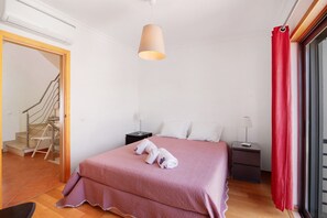 A bedroom with a bed, a nightstand, a lamp, a red curtain, and a staircase.