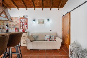A cozy living area with a sofa, a wooden ceiling, a kitchen area with a shelf of items, and a sliding door.