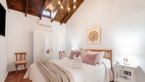 Un dormitorio con techo de madera, una cama con cabecera blanca, una mesita de noche con lámpara y un aire acondicionado de pared.