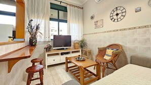 Ein gemütliches Wohnzimmer mit Fernseher, Holzmöbeln, einem Korbsessel und einem Fenster mit Vorhängen.