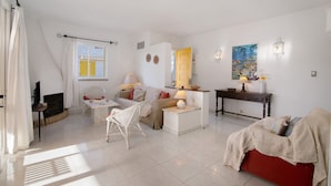 A living room with a sofa, a red couch, a white armchair, a fireplace, and a dining table. - Apartment 'Sail Golf Vilamoura' with Shared Pool, Wi-Fi and Air Conditioning (Quarteira)
