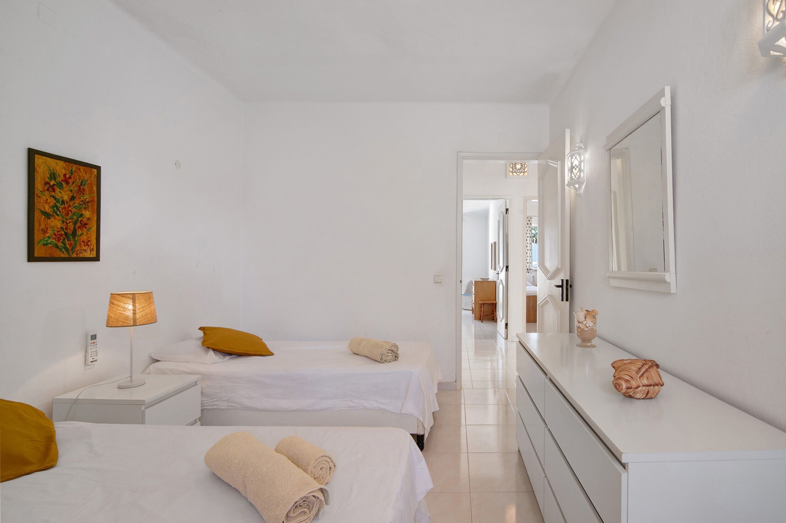 Habitación de hotel con dos camas, una mesita de noche con lámpara, un cuadro en la pared y un espejo sobre el tocador.