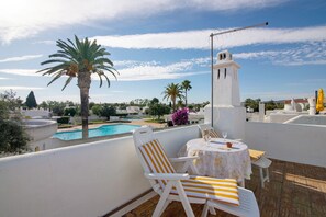 Une terrasse sur le toit avec une piscine, des chaises blanches, une table avec un verre et une structure en forme de tour blanche.