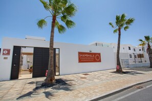 Un edificio moderno con un cartel que dice 'SHAMBHALA FUERTEVENTURA' y una puerta que da paso a un espacio interior.