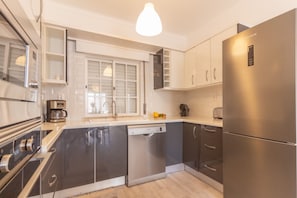 Una cocina moderna con lavavajillas, electrodomésticos de acero inoxidable y una ventana con persianas.