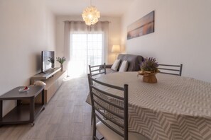Una sala de estar moderna con una mesa de comedor, sillas, un televisor, un sofá, una lámpara y un ventanal con cortinas.