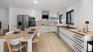 Una cocina moderna con armarios blancos, encimera de madera y una zona de comedor con sillas blancas.