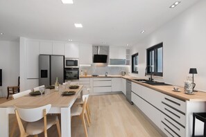 Una cocina moderna con armarios blancos, encimera de madera y una zona de comedor con sillas blancas.