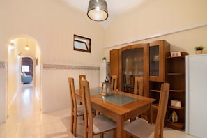Uma área de refeições com uma mesa e cadeiras de madeira, um armário com portas de vidro e um corredor que leva a outro quarto.