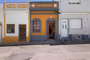 Um edifício com fachada distinta em amarelo e cinza, número 61, apresentando uma porta de madeira e janelas em arco.