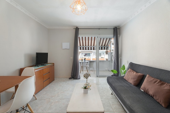 A modern living room with a sofa, a TV, a dining table, and a view of the outside.