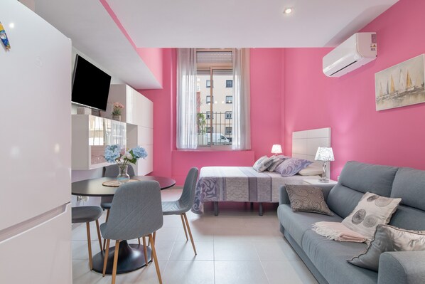 Eine moderne Wohnung mit einer Wand in Rosa, einem Bett, einem Sofa, einem Essbereich und einem Fernseher.