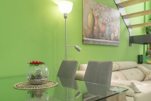 A green wall, a glass table with a vase, two chairs, a sofa, and a floor lamp.