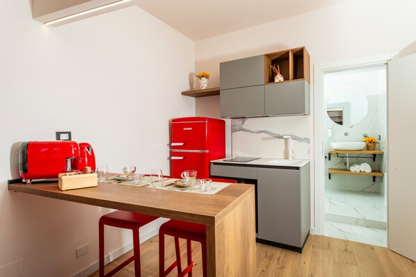 A compact kitchen with a wooden table, red chairs, a red refrigerator, and a grey countertop. - Apartment 'Home' with Balcony, Wi-Fi and Air Conditioning (Catania)
