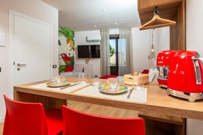 A modern kitchen with a dining table, chairs, a red coffee machine, and a TV mounted on the wall. - Apartment 'Home' with Balcony, Wi-Fi and Air Conditioning (Catania)