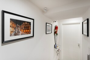 A hallway with a framed photograph of a building, a small framed picture, and a vase with flowers.