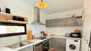 Une cuisine moderne équipée d’un lave-vaisselle, d’un four et d’un lave-linge, avec une fenêtre offrant une belle vue et un luminaire suspendu.