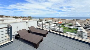 Une terrasse sur le toit avec deux chaises longues, une vue sur la mer et un panorama sur la ville au loin.