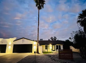 A modern house with a garage, a well-lit driveway, and a palm tree.