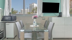 A modern kitchen with a glass dining table, white cabinets, a microwave, and a TV mounted on the wall.
