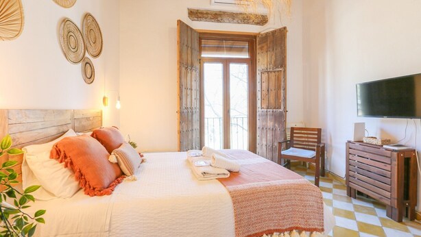 A neatly arranged bedroom with a bed, bedside table, chair, and a television.