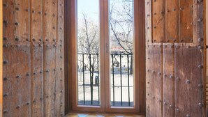 A wooden door with metal studs and a metal gate, leading to an outdoor area with trees and a fence.