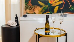 Una botella de vino y dos copas sobre una mesa redonda, una toalla en un taburete negro, y un cuadro al fondo.