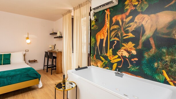 Una habitación con cama, escritorio, sillón, bañera y un mural temático de jungla en la pared.