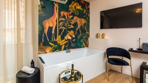Un baño moderno con una bañera grande, un televisor de pared y un mural con temática tropical.