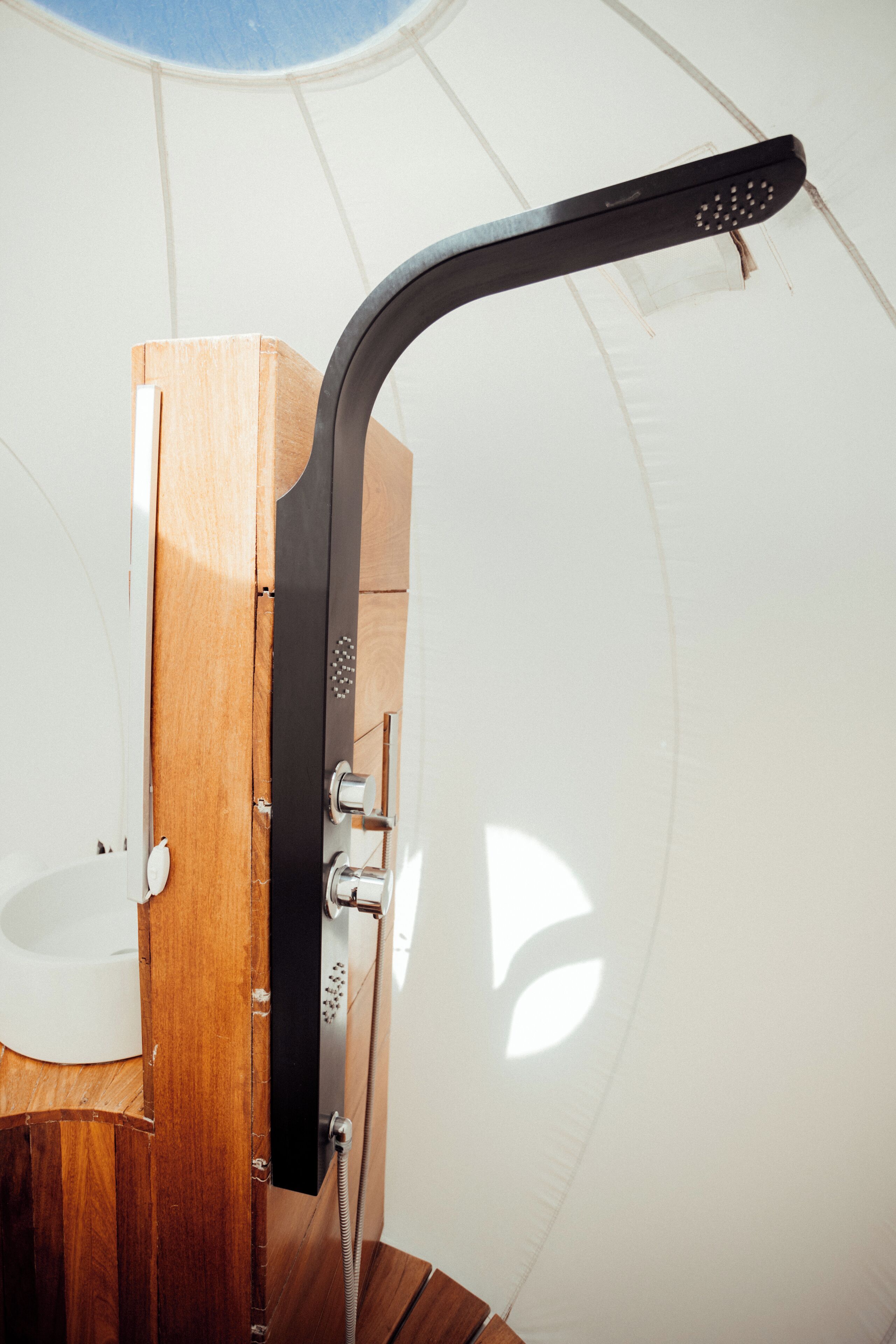 Een kleine badkamer met een houten wastafelmeubel, een witte wasbak en een zwarte douchekop.