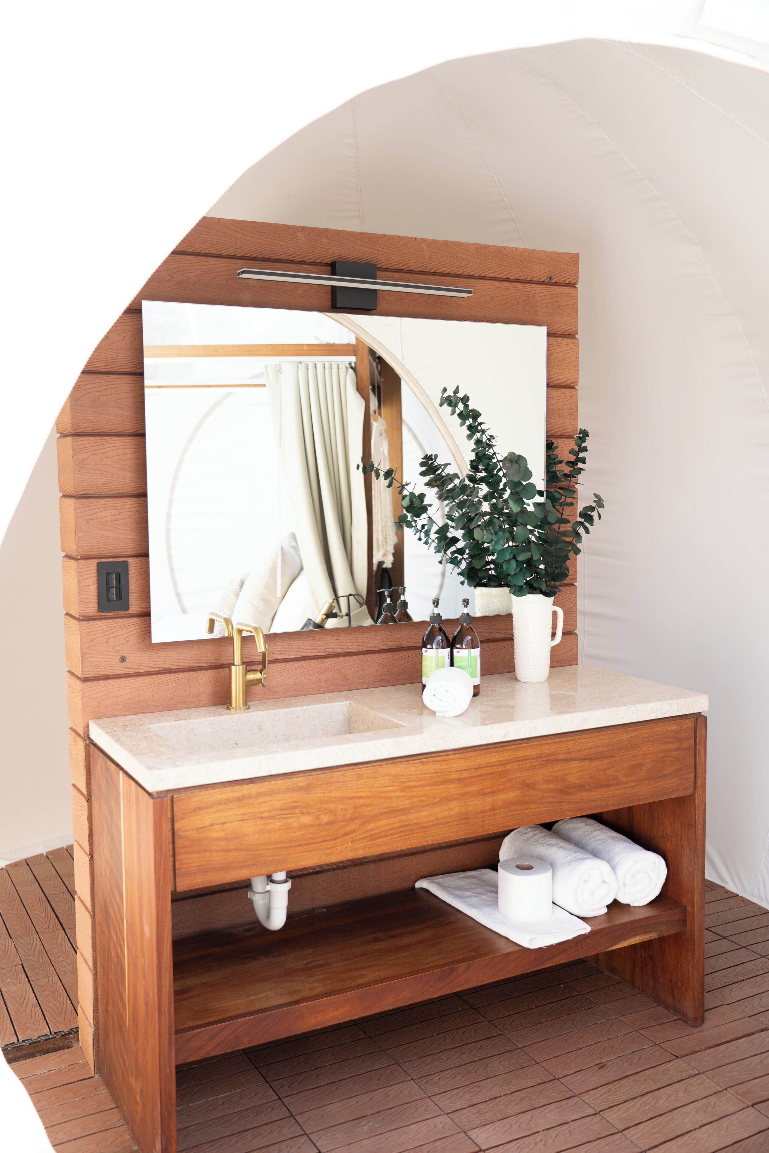Une coiffeuse en bois avec un miroir, un lavabo et une plante en pot.