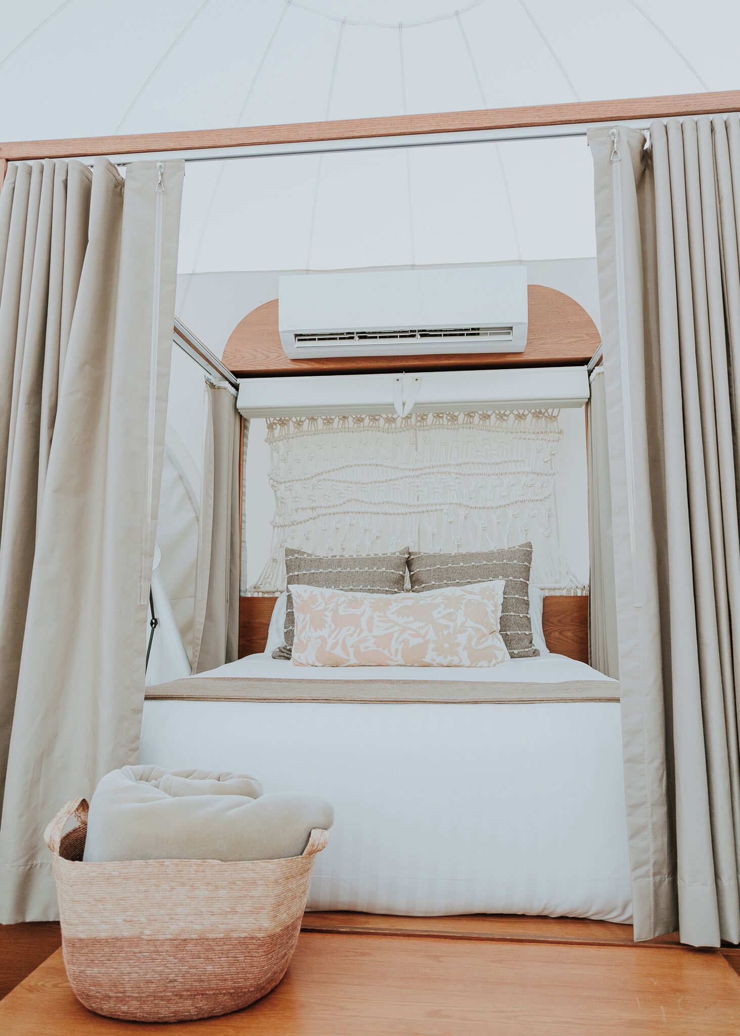 A bed with a canopy, a wall-mounted air conditioner, and a woven basket on the floor.
