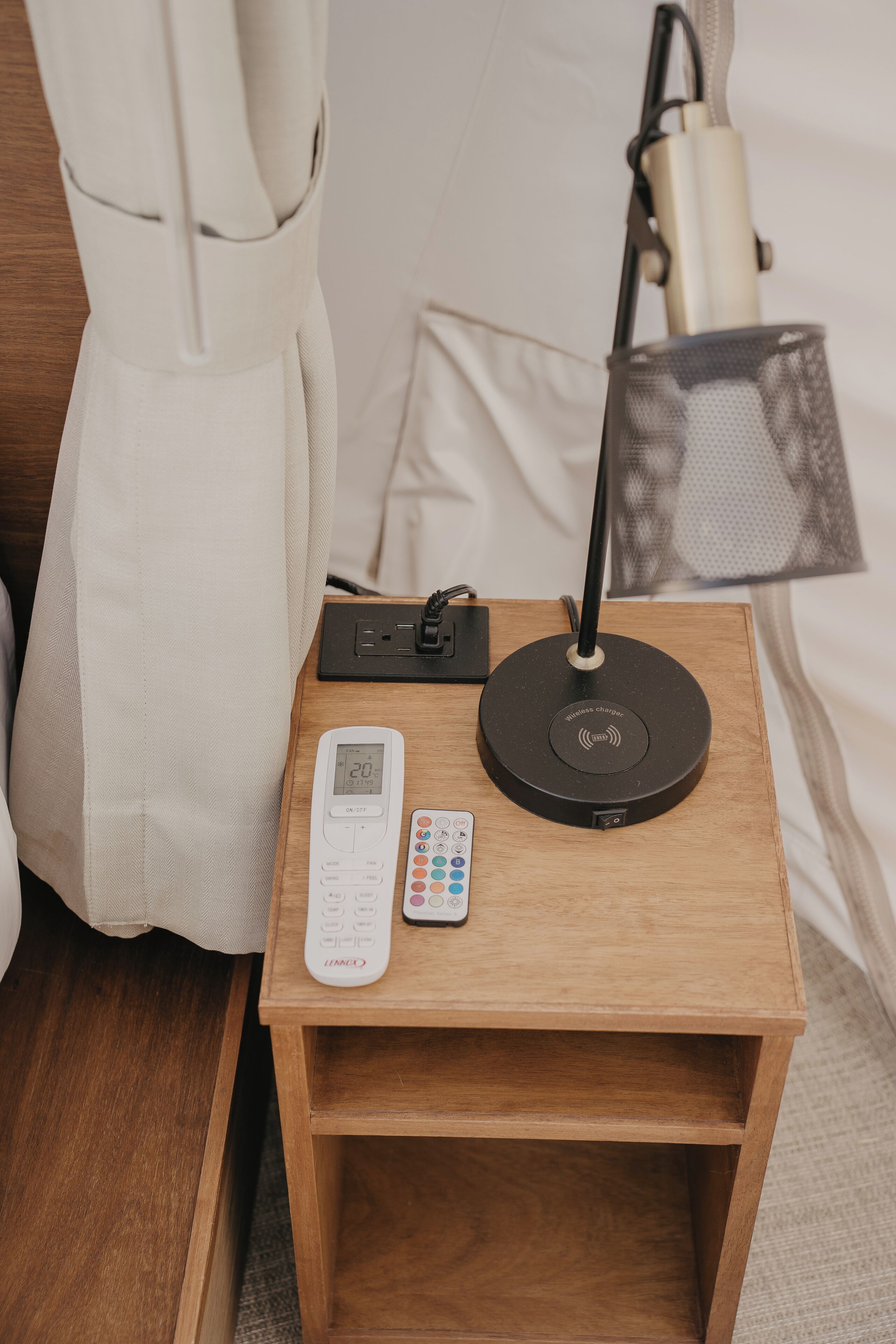 Una mesita de noche de madera con un control remoto, un alargador y una lámpara.
