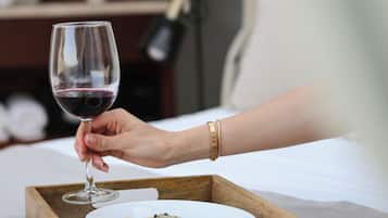 A hand holding a wine glass over a wooden tray with a bowl of food.