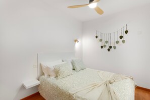 A bedroom with a bed, a ceiling fan, a wall-mounted light, and a wall decoration.