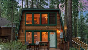 A two-story log cabin with a green exterior, a front porch with a bench, and a staircase leading to the entrance. - Drifthaus - Large Deck w/ Firepit, Mountain Views (Homewood)