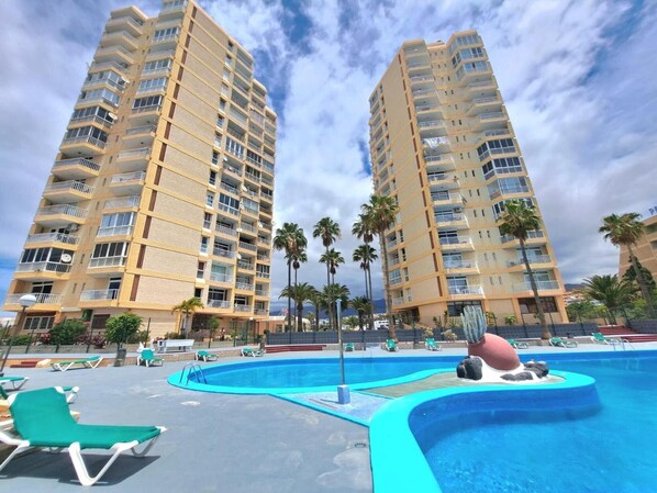Un hotel con piscina, varios balcones y palmeras.
