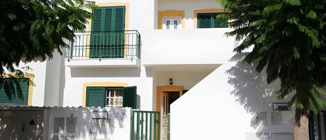 A two-story building with a white facade, green shutters, and a gated entrance.