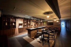 Eine Bar mit einer Theke und Sitzgelegenheiten. Regale mit Flaschen und Gläsern sind sichtbar.