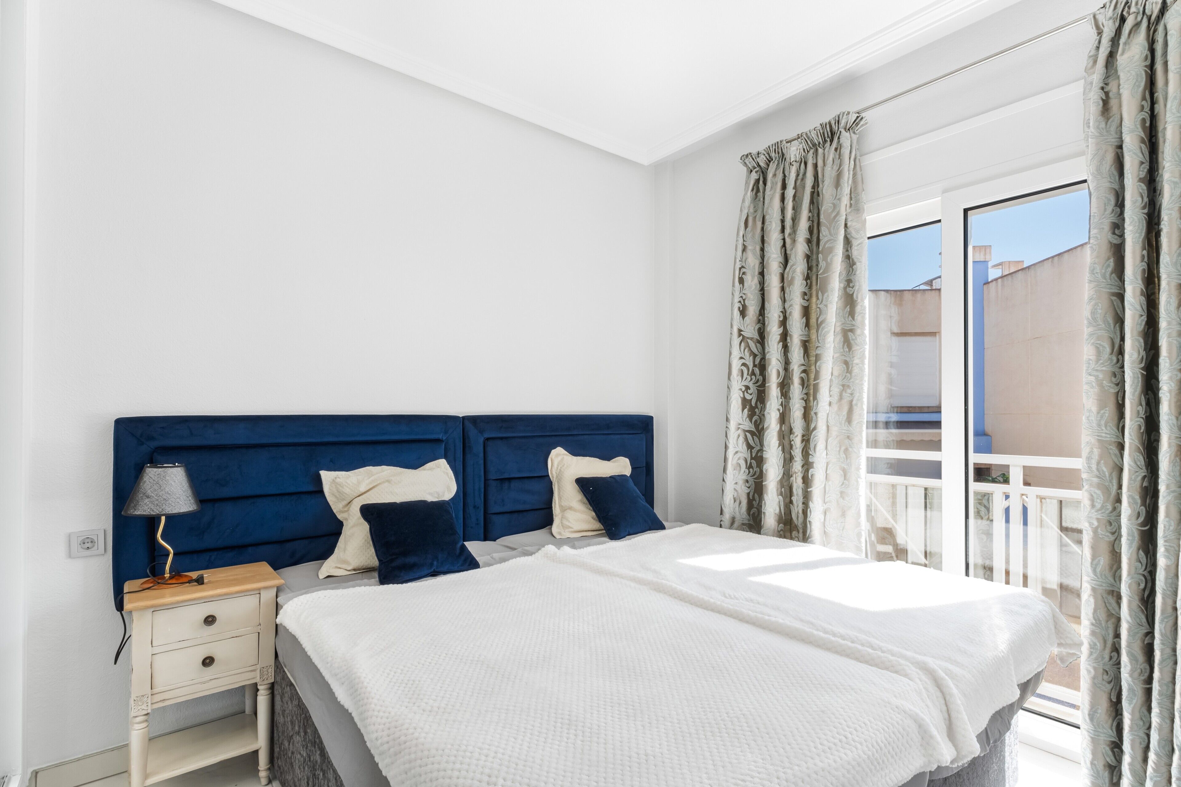 A bedroom with a bed, nightstand, lamp, and curtains.