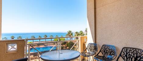 A balcony with a pool view, metal chairs, and a round table.